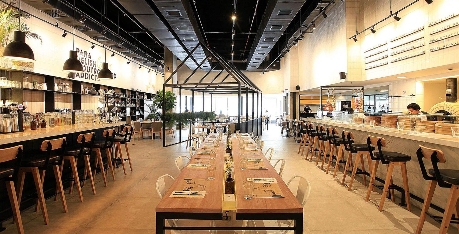 Sal&atilde;o de um restaurante contempor&acirc;neo com mesa comunit&aacute;ria e balc&atilde;o