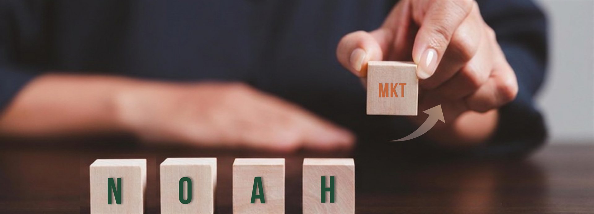 Blocos de madeira formando NOAH, com uma m&atilde;o posicionando o bloco MKT